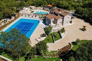 Ein großes Haus mit Schwimmbad, Tennisplatz und einem gepflegten Garten.