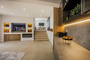 Ein modernes Wohnzimmer mit Flachbildfernseher, Holzelementen und einer Treppe, die in eine obere Ebene führt.