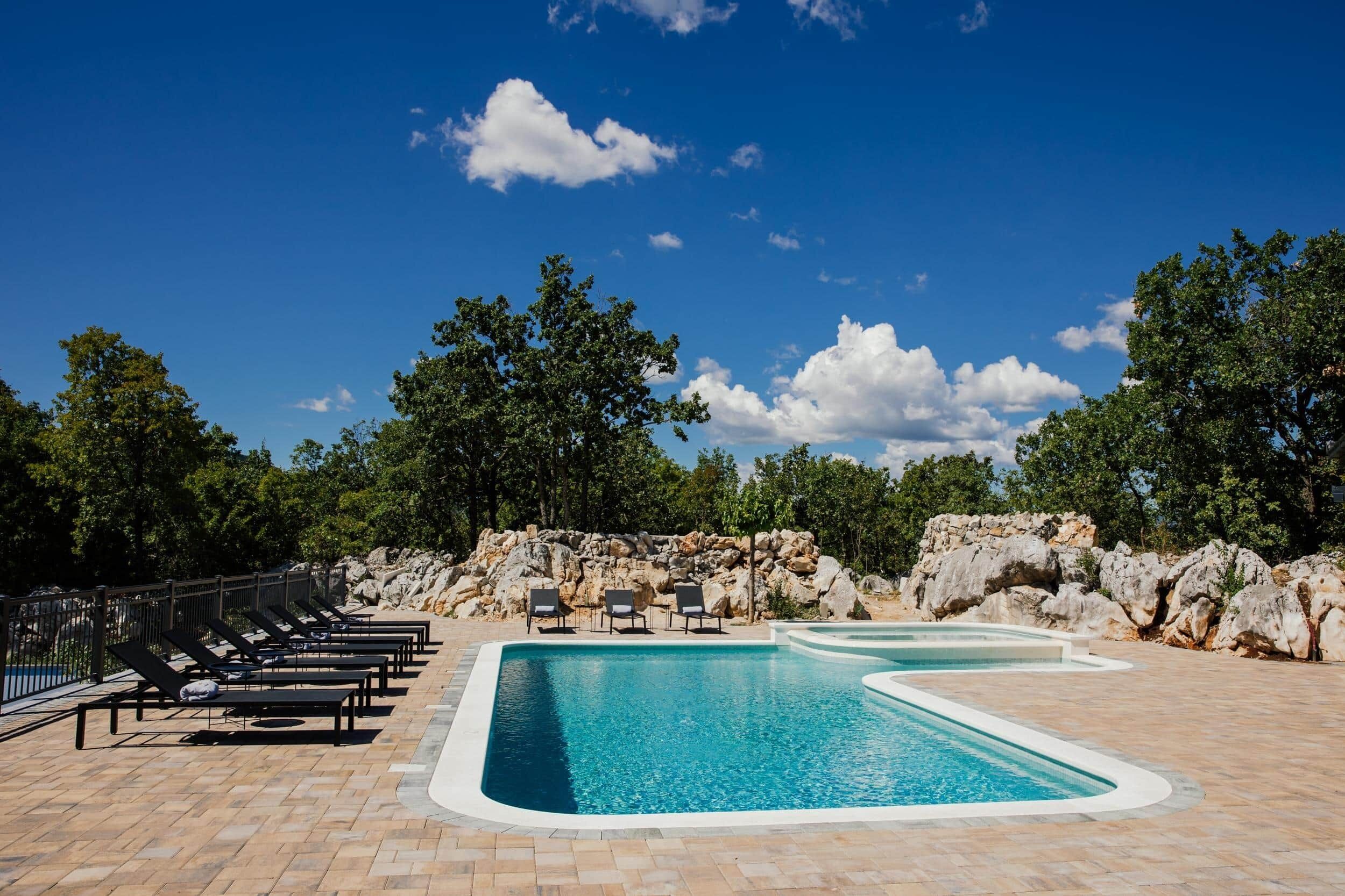 Une piscine avec des chaises longues et un mur en pierre.
