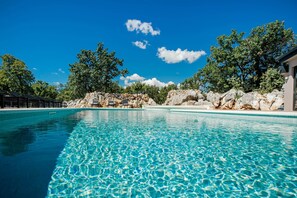 Una piscina cristallina blu con lettini e uno sfondo roccioso.