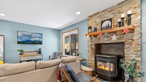 A living room with a stone fireplace, a sofa, a wooden chair, and a 'Welcome' sign.