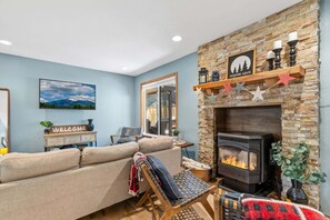 Una sala de estar con chimenea de piedra, un sofá, una silla de madera y un cartel que dice 'Welcome'.