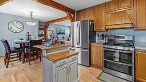 A kitchen with wooden cabinets, a stainless steel refrigerator, a stove, and a dining area with a table and chairs.