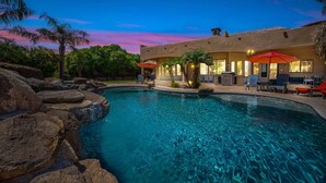 A swimming pool with rocks, palm trees, and a building with outdoor seating and umbrellas. - 104th Mesa 1331 Paradise Found (Mesa)