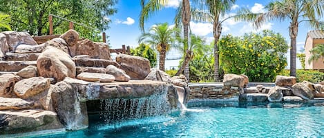 A pool with a waterfall feature surrounded by rocks and palm trees.