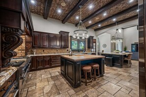 A spacious kitchen with dark wood cabinets, a large island with stools, a built-in oven, and a herringbone ceiling. - 104th Mesa 1331 Paradise Found (Mesa)