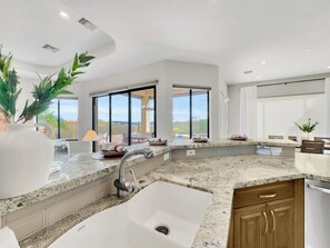 A modern kitchen with granite countertops, a stainless steel sink, and large windows offering a view of the outdoors. - Golden Eagle Fountain Hills (Fountain Hills)