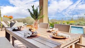 Un área de comedor al aire libre con una piscina de fondo.
