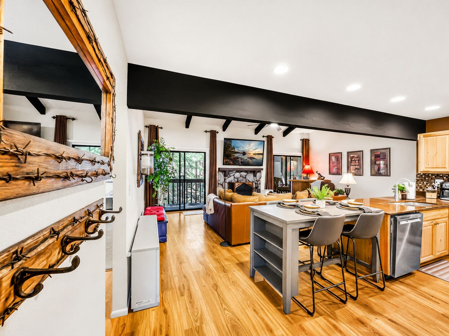 A modern kitchen with a central island, wooden flooring, and a black ceiling beam.