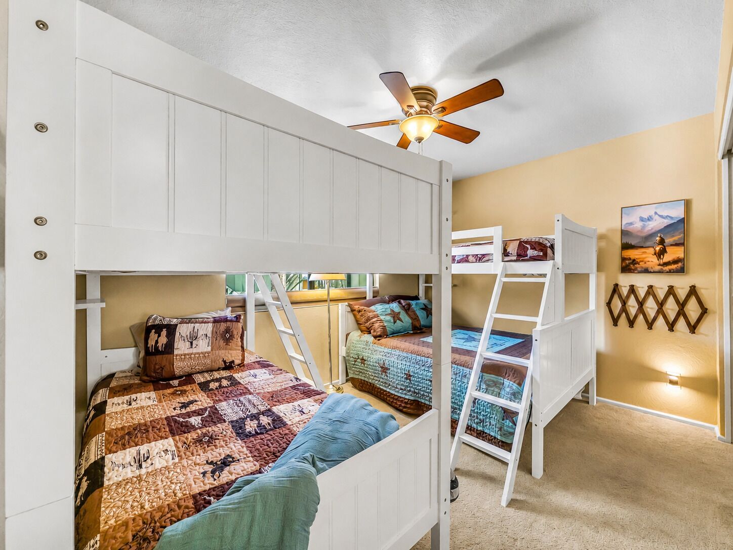A bunk bed room with a ceiling fan, a ladder, and a painting on the wall.