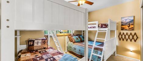A bunk bed room with a ceiling fan, a ladder, and a painting on the wall.