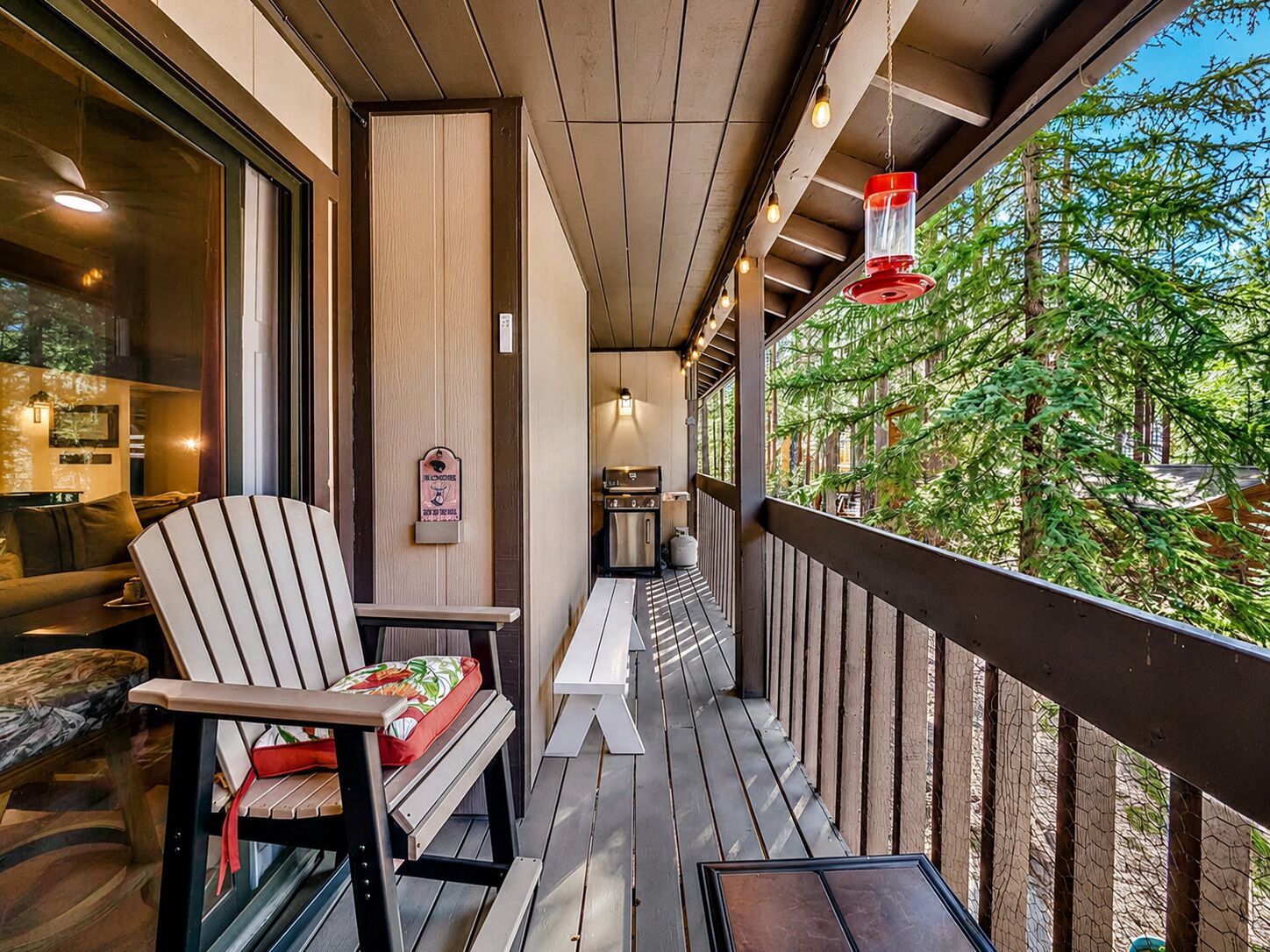 A wooden deck with outdoor seating, a grill, and a view of trees.