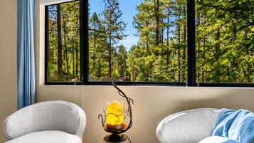 A room with a large window, two armchairs, a small wooden table, and a decorative candle.