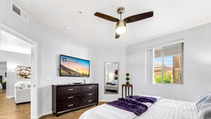 Un dormitorio con cama, televisor, ventilador de techo, cómoda y ventana.