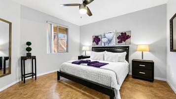A bedroom with a bed, two bedside tables, a ceiling fan, a window, and artwork on the wall.