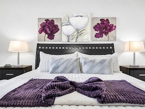 A neatly made bed with a purple blanket, two bedside lamps, and three framed artworks above it. - Southern #1083 Mesa (Mesa)