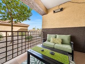 A balcony with a green sofa, a table with decorative items, and a view of buildings and a tree. - Southern #1083 Mesa (Mesa)