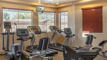 A gym with four treadmills, a TV mounted on the wall, and large windows with blinds.