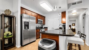 Cocina moderna con electrodomésticos de acero inoxidable, armarios de madera y una isla central con taburetes de bar.