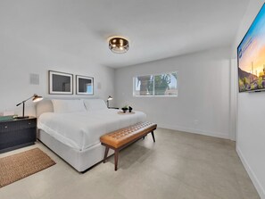 A bedroom with a bed, bedside tables, a bench, a ceiling light, a window with blinds, and a wall-mounted TV. - Captain Dreyfus Phoenix (Phoenix)