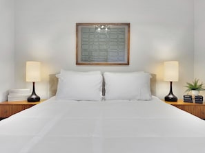 A neatly made bed with white linens, two bedside lamps, a framed artwork above the bed, and a small potted plant on the nightstand. - Captain Dreyfus Phoenix (Phoenix)