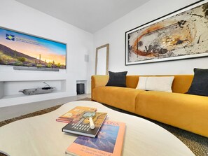 A modern living room with a sofa, a coffee table with books, a TV, and a large abstract painting. - Captain Dreyfus Phoenix (Phoenix)