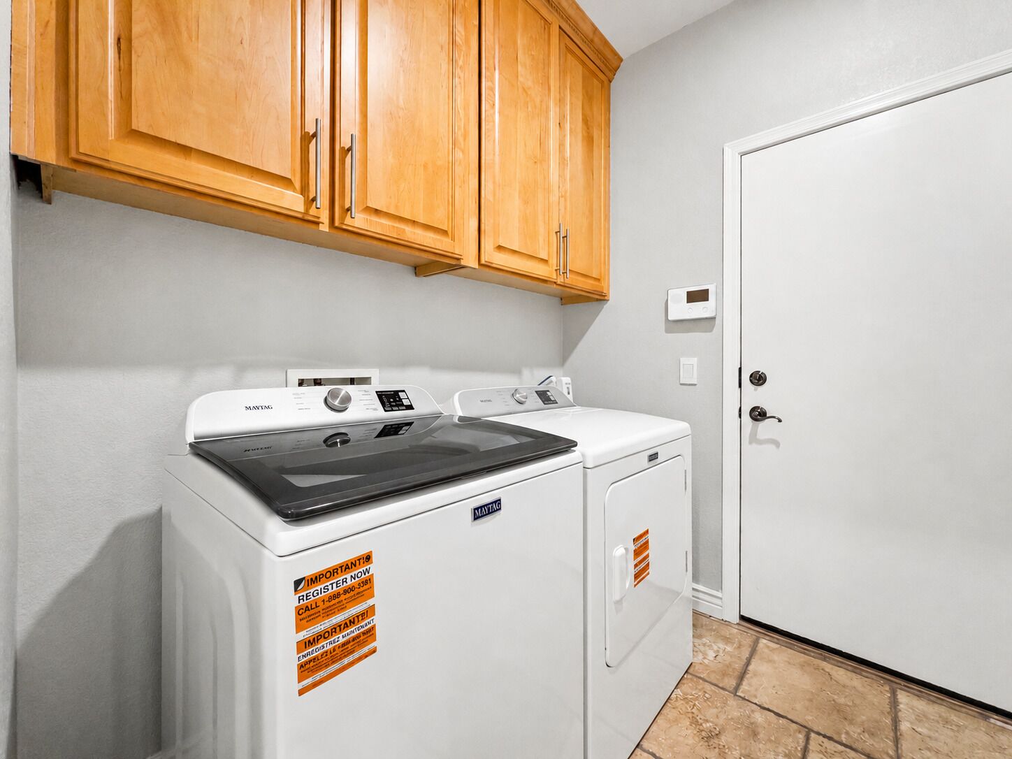 A laundry room with a washing machine, dryer, and wooden cabinets.