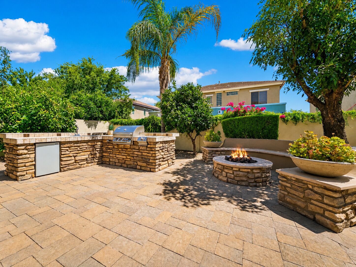 Une terrasse extérieure dotée d’un barbecue en pierre, d’un foyer et d’un réfrigérateur encastré.