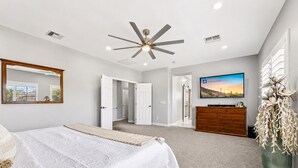 A bedroom with a bed, a ceiling fan, a dresser, a TV, and a large mirror. - The Jade House Queen Creek (Queen Creek)