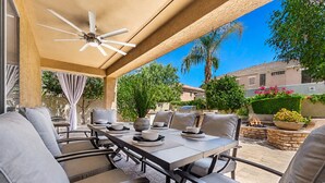 An outdoor patio with a table set for dining, surrounded by cushioned chairs, a ceiling fan, and a view of the neighborhood. - The Jade House Queen Creek (Queen Creek)