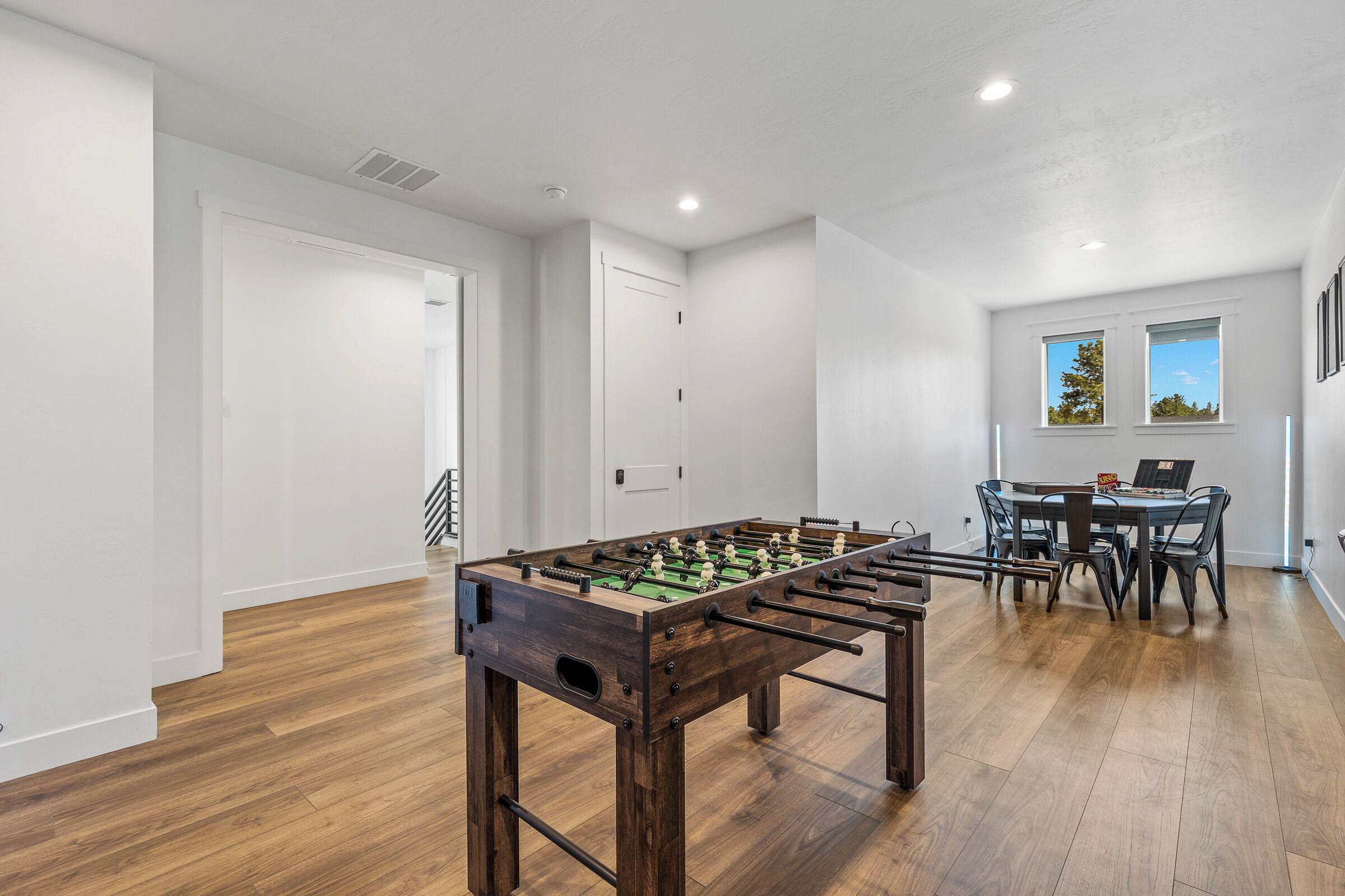 Um quarto com mesa de pebolim, uma mesa de jantar com cadeiras e uma janela com vista para árvores.