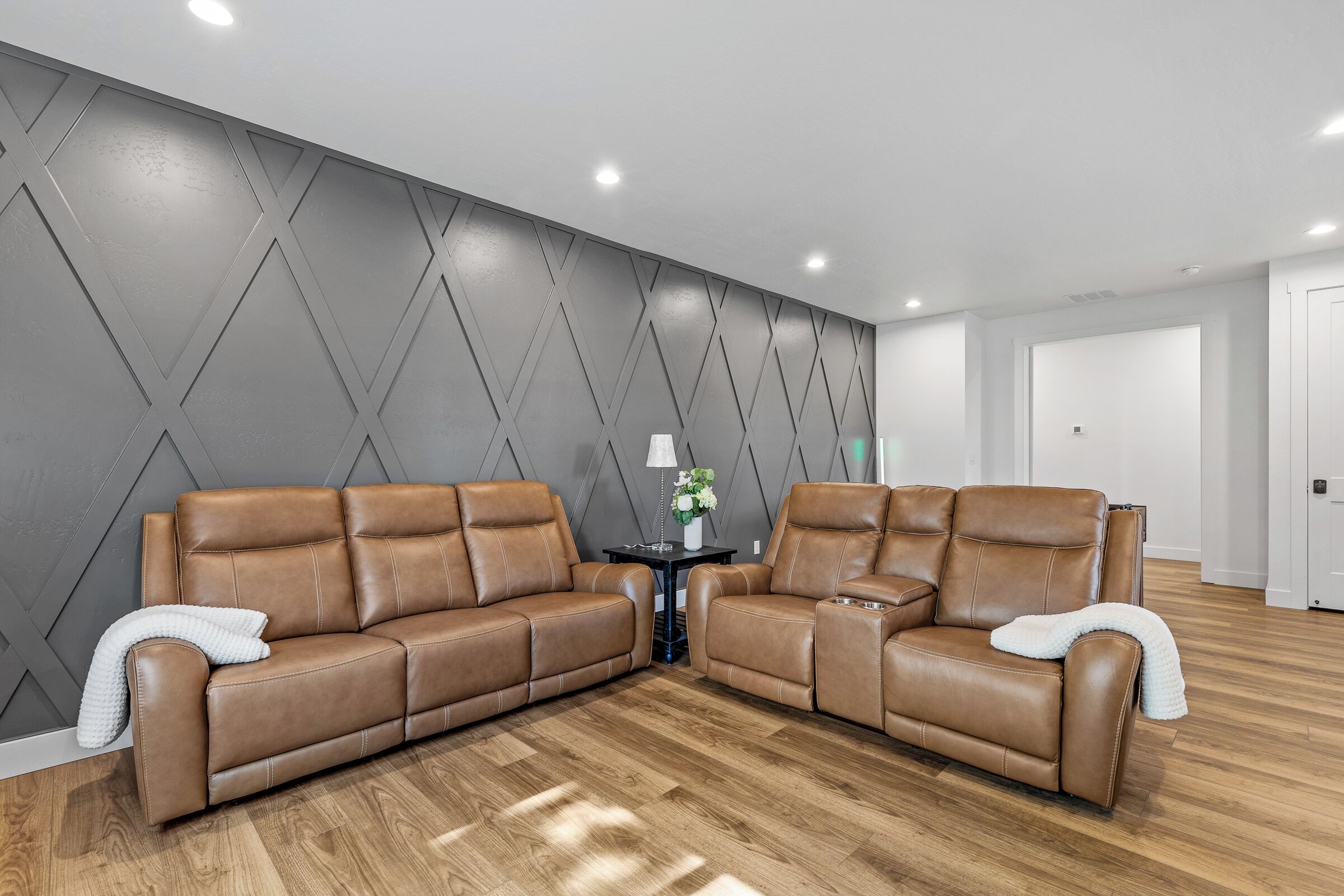 A modern living room with two brown leather sofas, a small table with a lamp, and a grey geometric wall.