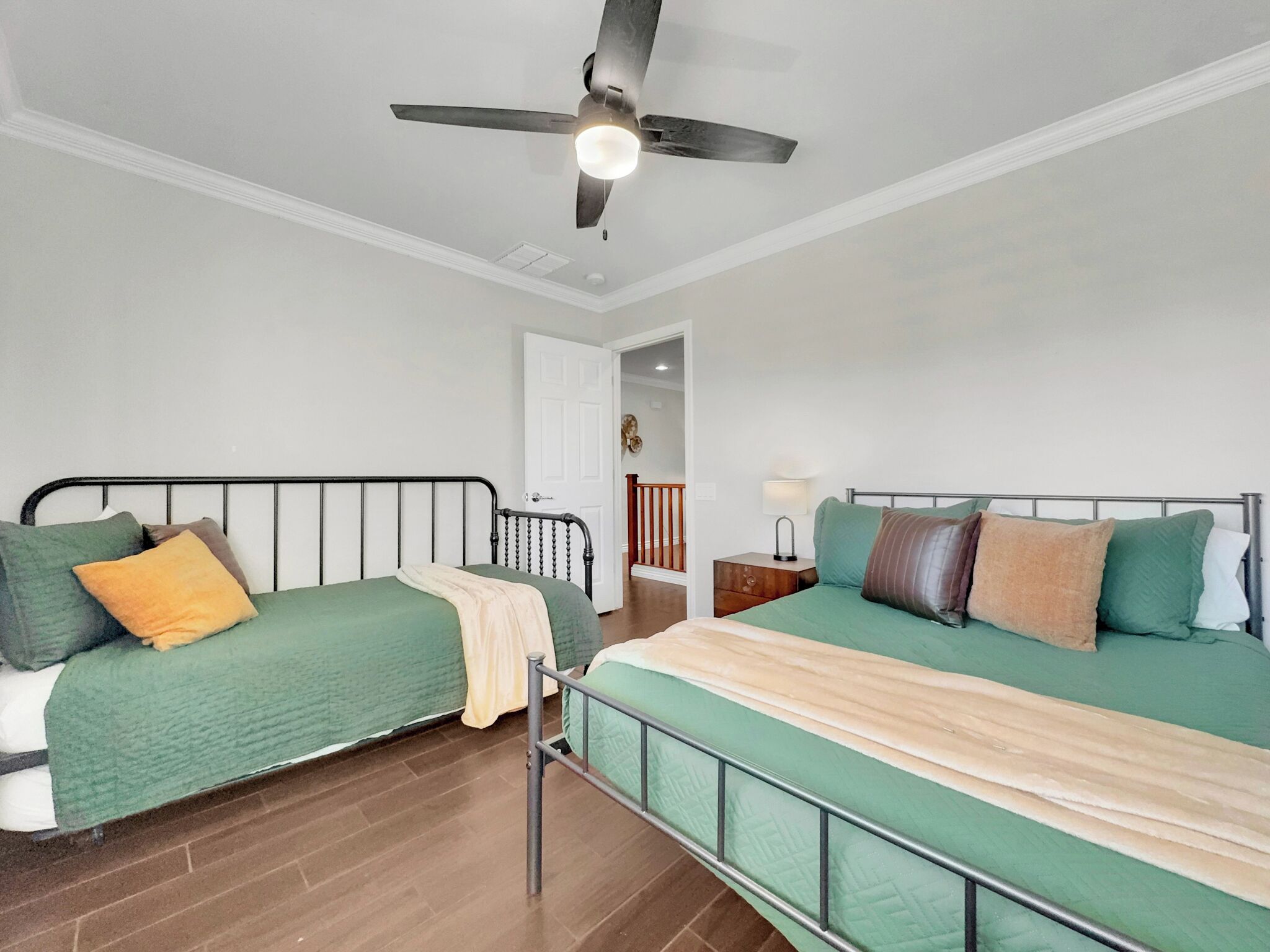 A bedroom with two beds, a ceiling fan, a nightstand, and a door leading to another room.