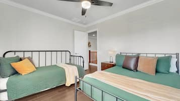 A bedroom with two beds, a ceiling fan, a nightstand, and a door leading to another room.