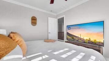 A bedroom with a bed, a ceiling fan, a TV, and a door leading to another room.