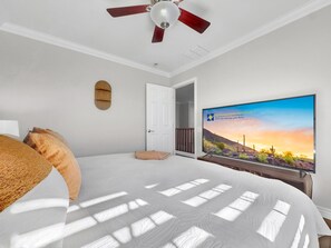 Une chambre à coucher avec un lit, un ventilateur de plafond, une télévision et une porte donnant sur une autre pièce.
