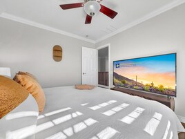 A bedroom with a bed, a ceiling fan, a TV, and a door leading to another room.