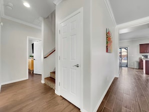 A spacious hallway with hardwood flooring, white walls, and a white door. A staircase with a wooden handrail leads to another level. - Magic of Maricopa (Maricopa)