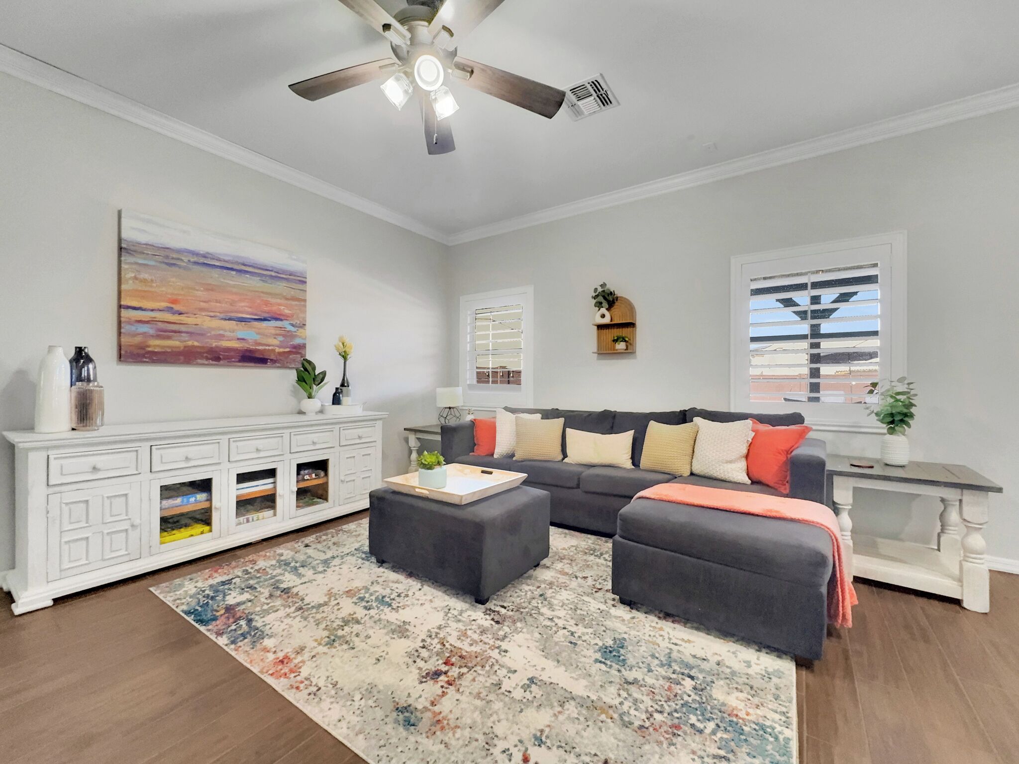 A living room with a ceiling fan, a sofa set, a white cabinet, and a colorful rug.