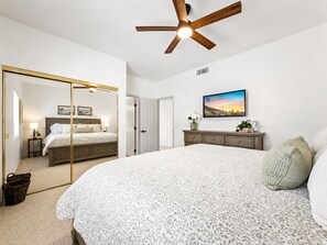 Un dormitorio con una cama grande, ventilador de techo, televisor y espejo.