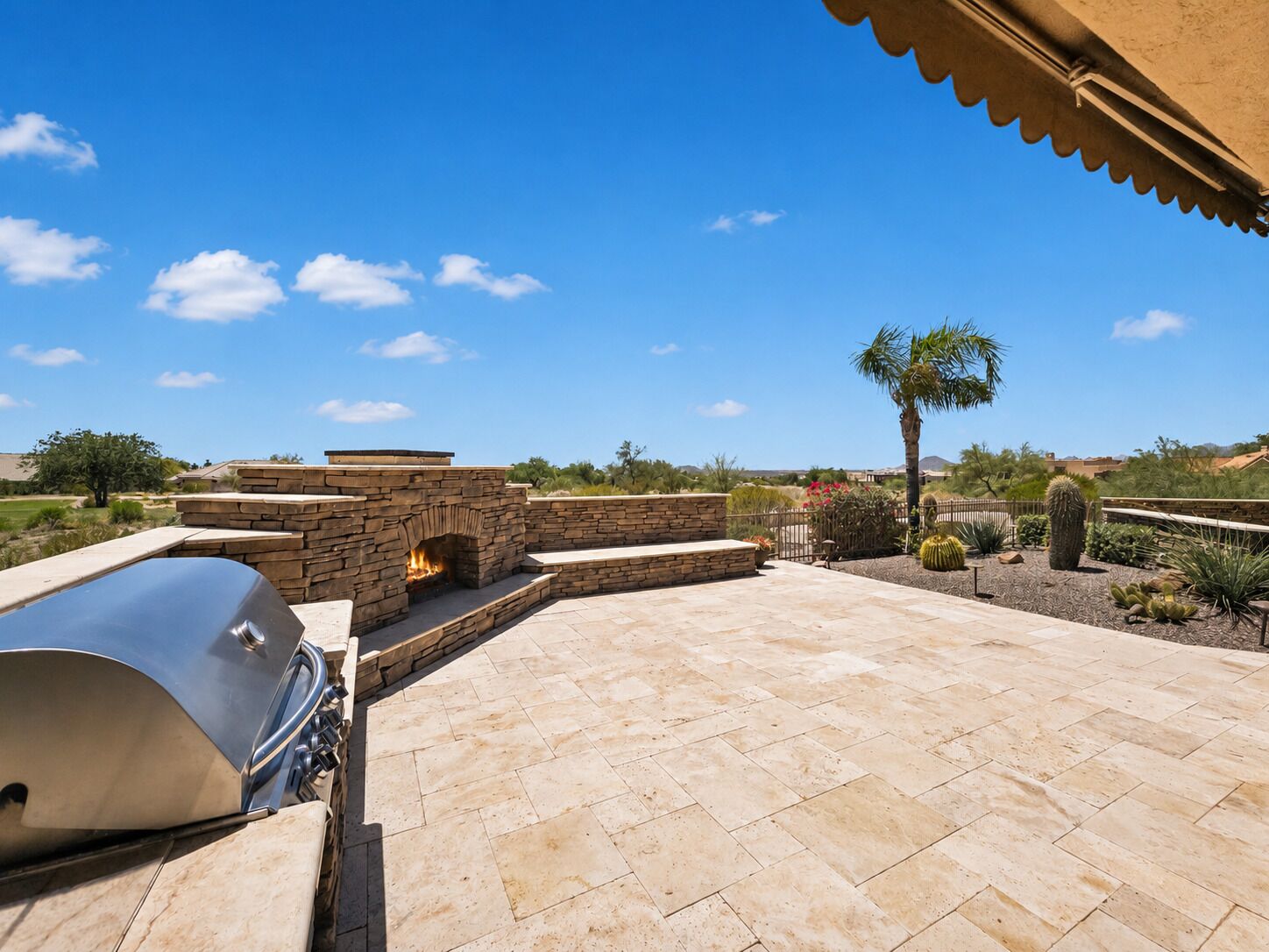 A patio with a stone fireplace, a grill, and a view of a desert landscape.