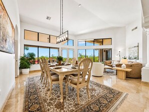 A spacious living area with a dining table, chairs, and a sofa. There are large windows offering a view of the outdoors. - Trailridge Mesa (Mesa)