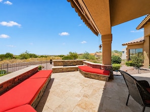 A covered patio with stone seating, a wicker chair, and a view of a residential area. - Trailridge Mesa (Mesa)