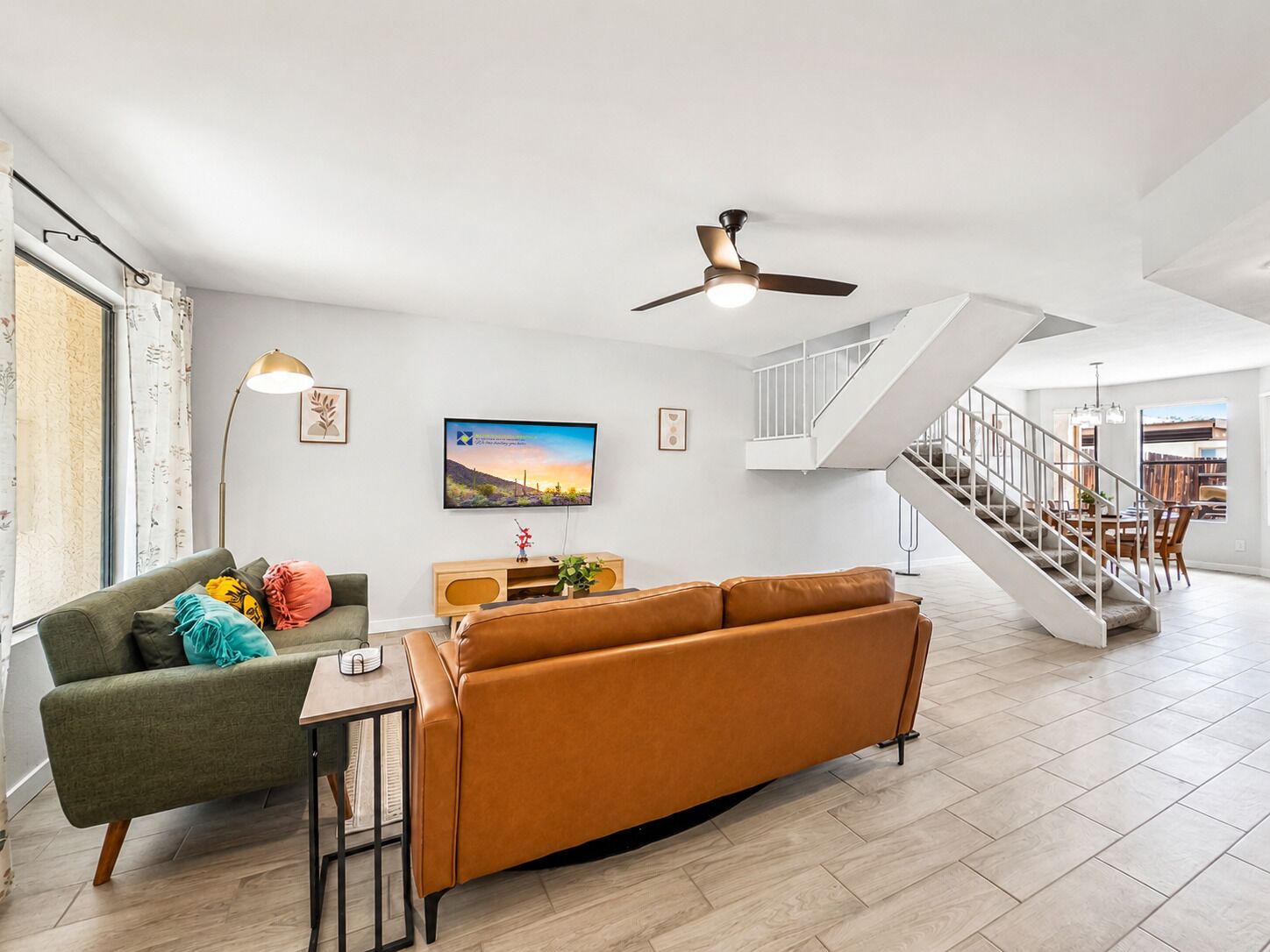 A spacious living area with a sofa, a coffee table, a TV, and a staircase leading to another room.