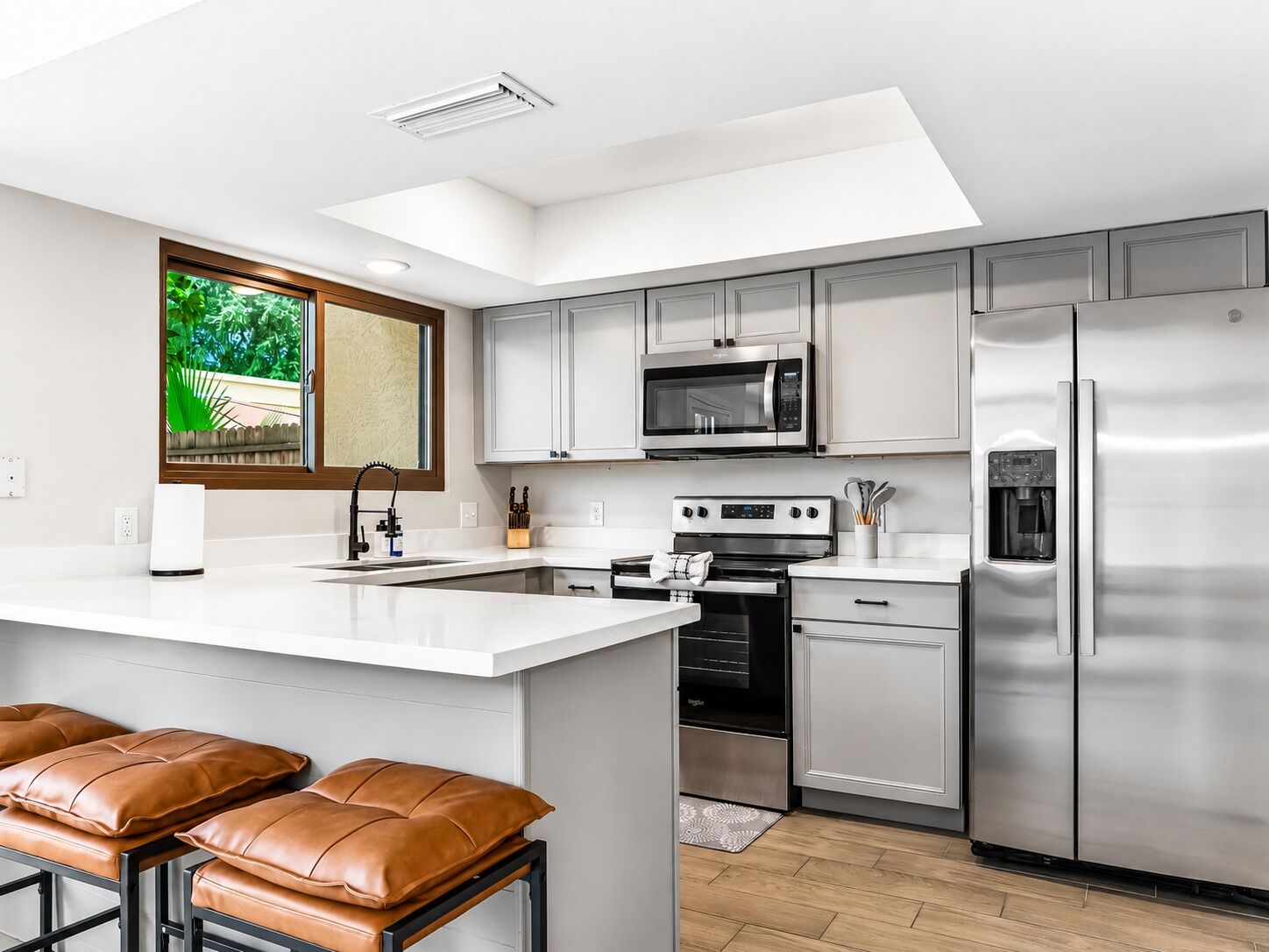 Uma cozinha moderna com ilha central, eletrodomésticos de aço inoxidável e uma janela com vista para o verde.
