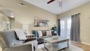 A living room with a gray sofa, a coffee table, a painting on the wall, a ceiling fan, and a window with curtains. - Southern #2059 Mesa (Mesa)