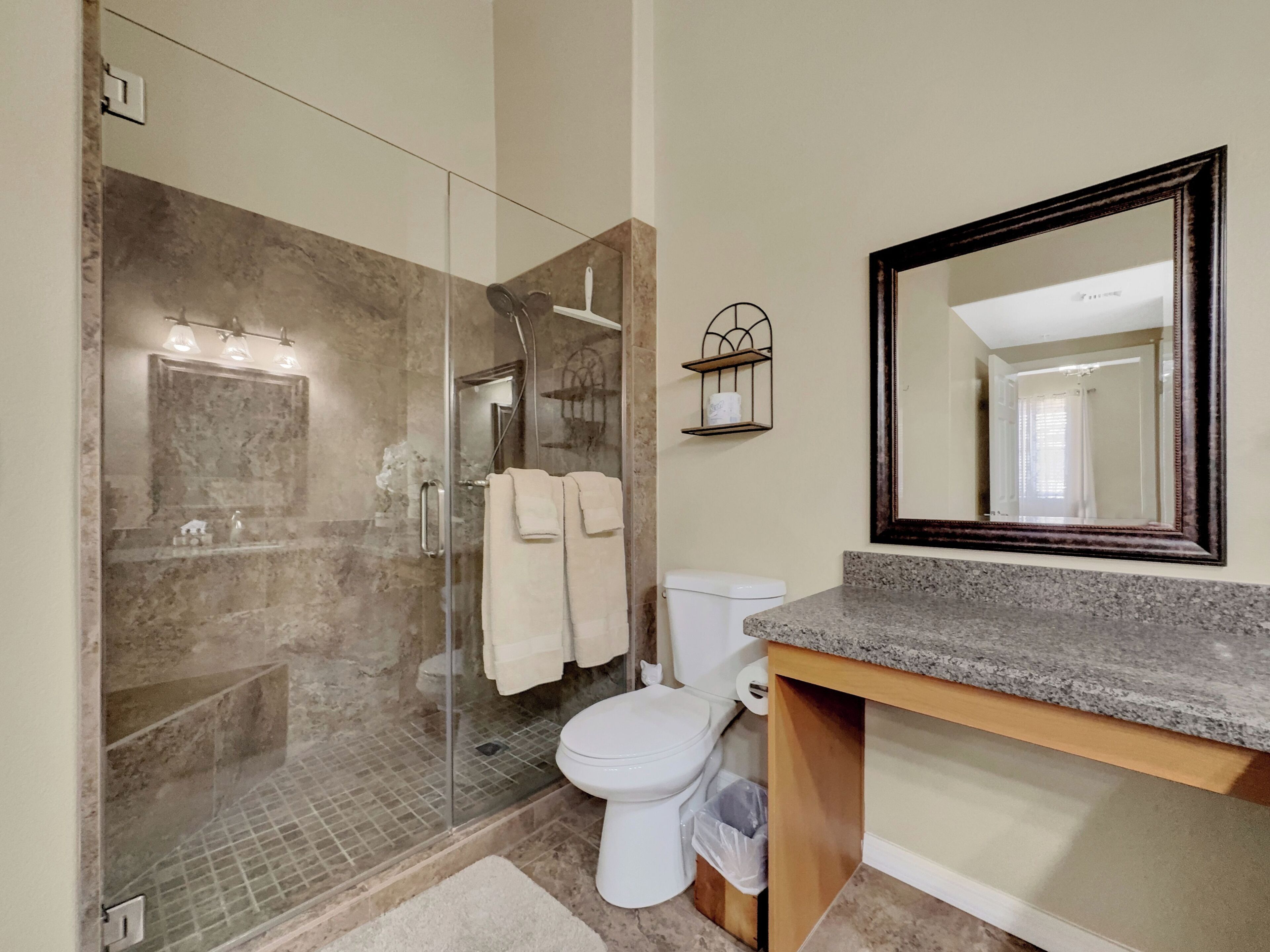 A modern bathroom with a glass-enclosed shower, a toilet, a sink with a granite countertop, and a large mirror.