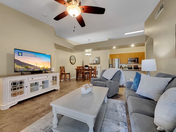 Una sala de estar con televisor, ventilador de techo, comedor y cocina.