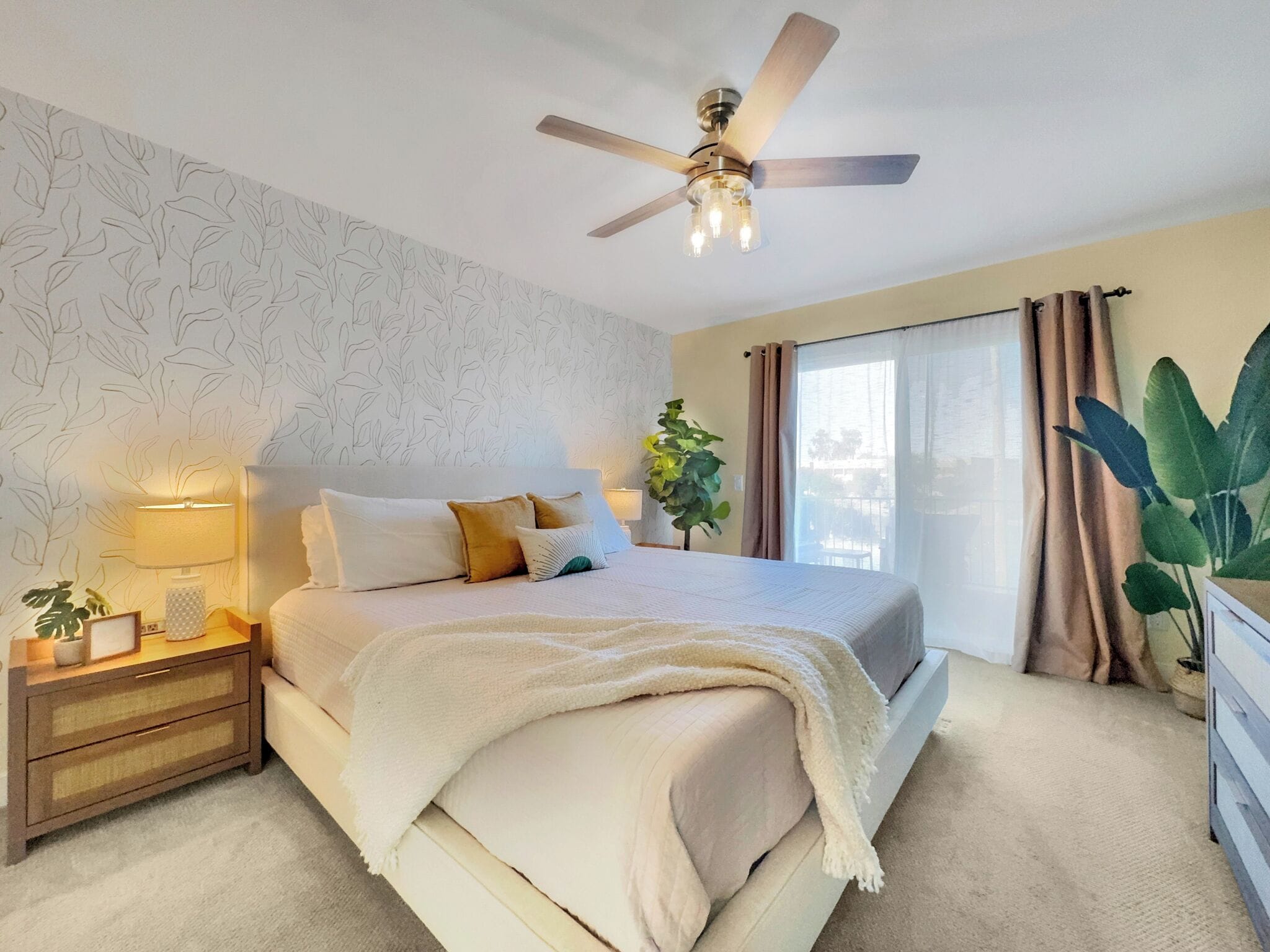 A bedroom with a bed, bedside table, lamp, and a ceiling fan.