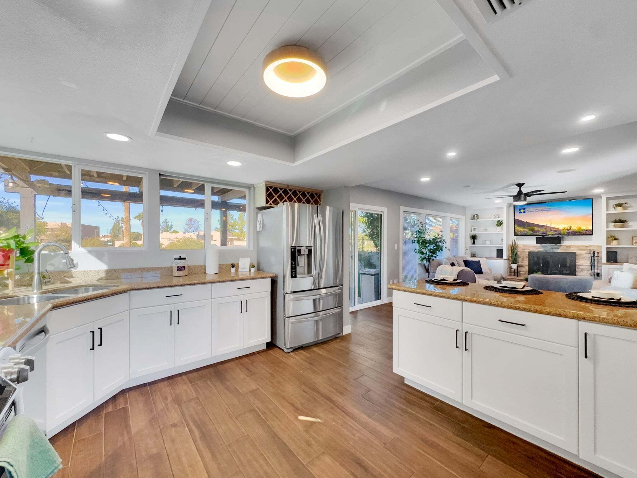 A modern kitchen with white cabinets, a stainless steel refrigerator, and a large window.